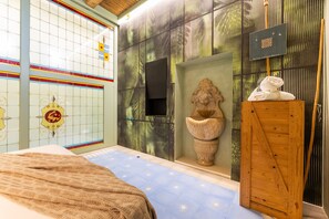 Ein Zimmer mit einem Bett, einem Holzkasten, einer Wand mit Dekoration und einem kleinen Tisch mit einem Handtuch.
