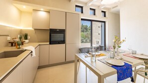 A modern kitchen with a built-in oven, a dining area with a table set for two, and a view of the outdoors through a window. - Ultra-Lux Tower Villa: Dual Pools, Near Beaches (Gallipoli)