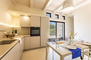 Eine moderne Küche mit Einbauofen, ein Essbereich mit Tisch für zwei Personen und ein Ausblick ins Freie durch ein Fenster.