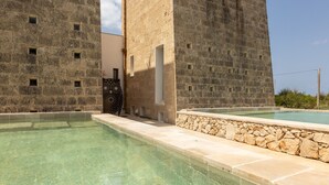 A swimming pool with clear water, surrounded by stone walls and a modern building with multiple windows. - Ultra-Lux Tower Villa: Dual Pools, Near Beaches (Gallipoli)