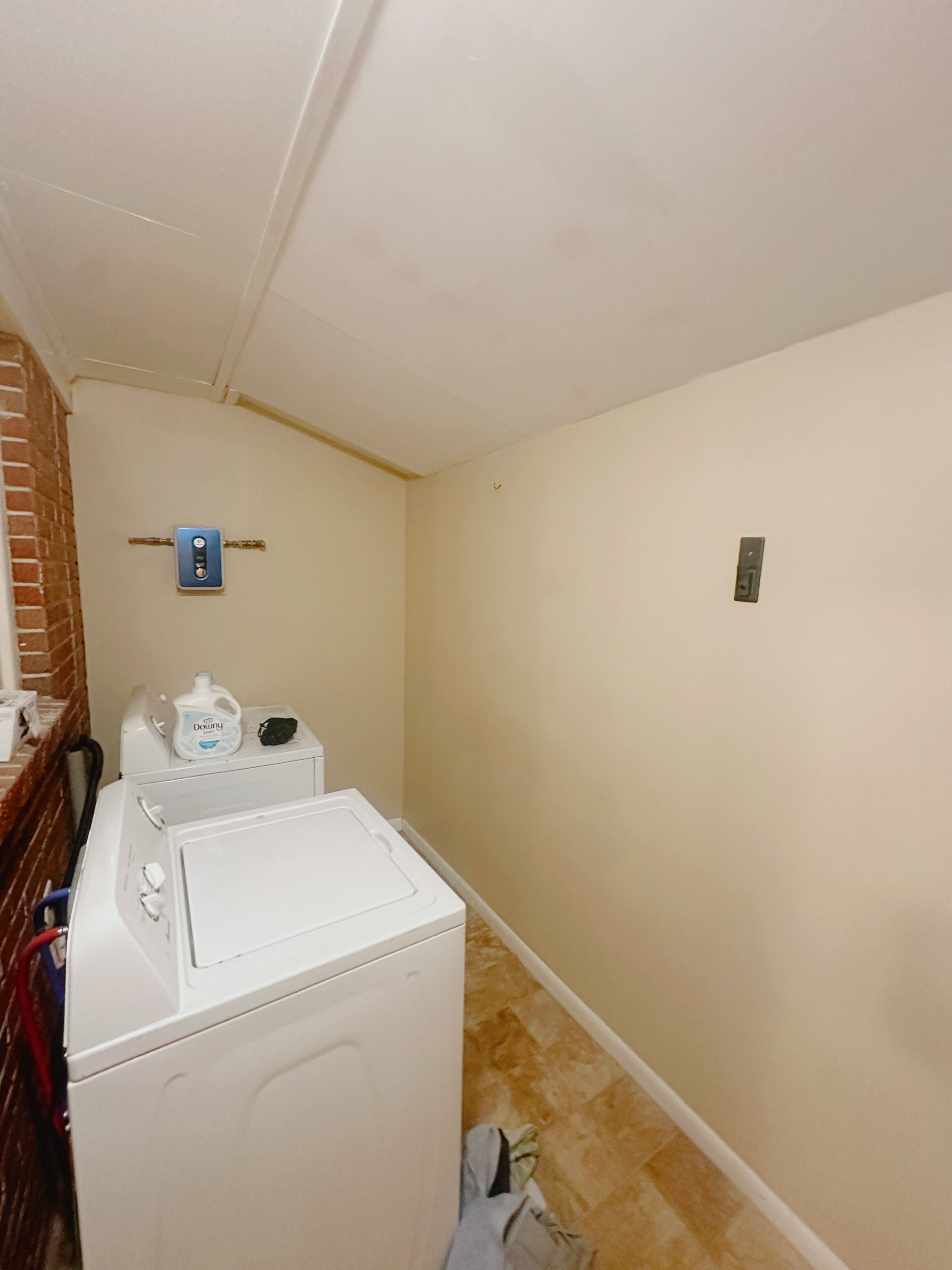 A laundry room with a dryer and washing machine, a brick wall, and a ceiling with a light fixture.