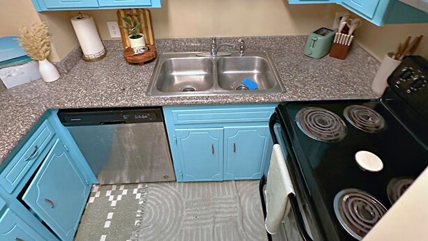 Una cocina con gabinetes azules, lavavajillas, estufa y un tapete estampado.