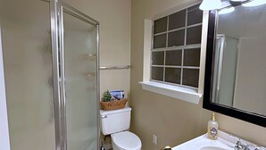 Un baño con ducha, inodoro, lavabo y un ventanal sobre el lavabo.