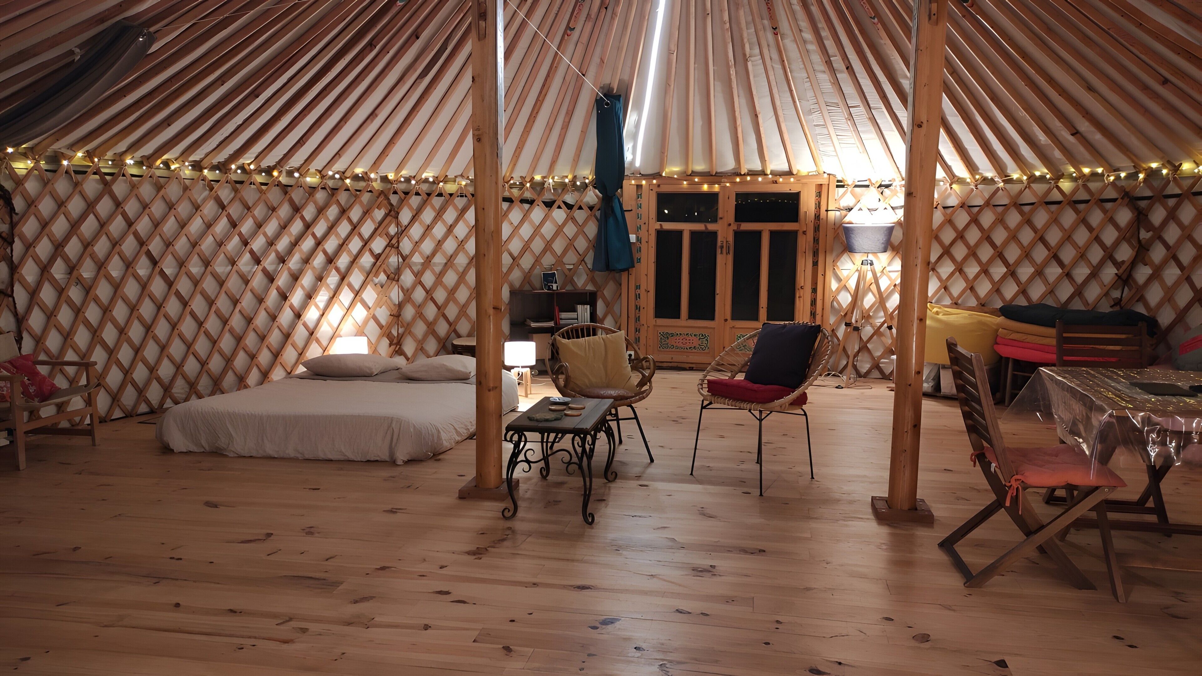 Ein gemütliches Innere einer Jurte mit einem Bett, einer Sitzecke und einem kleinen Tisch.