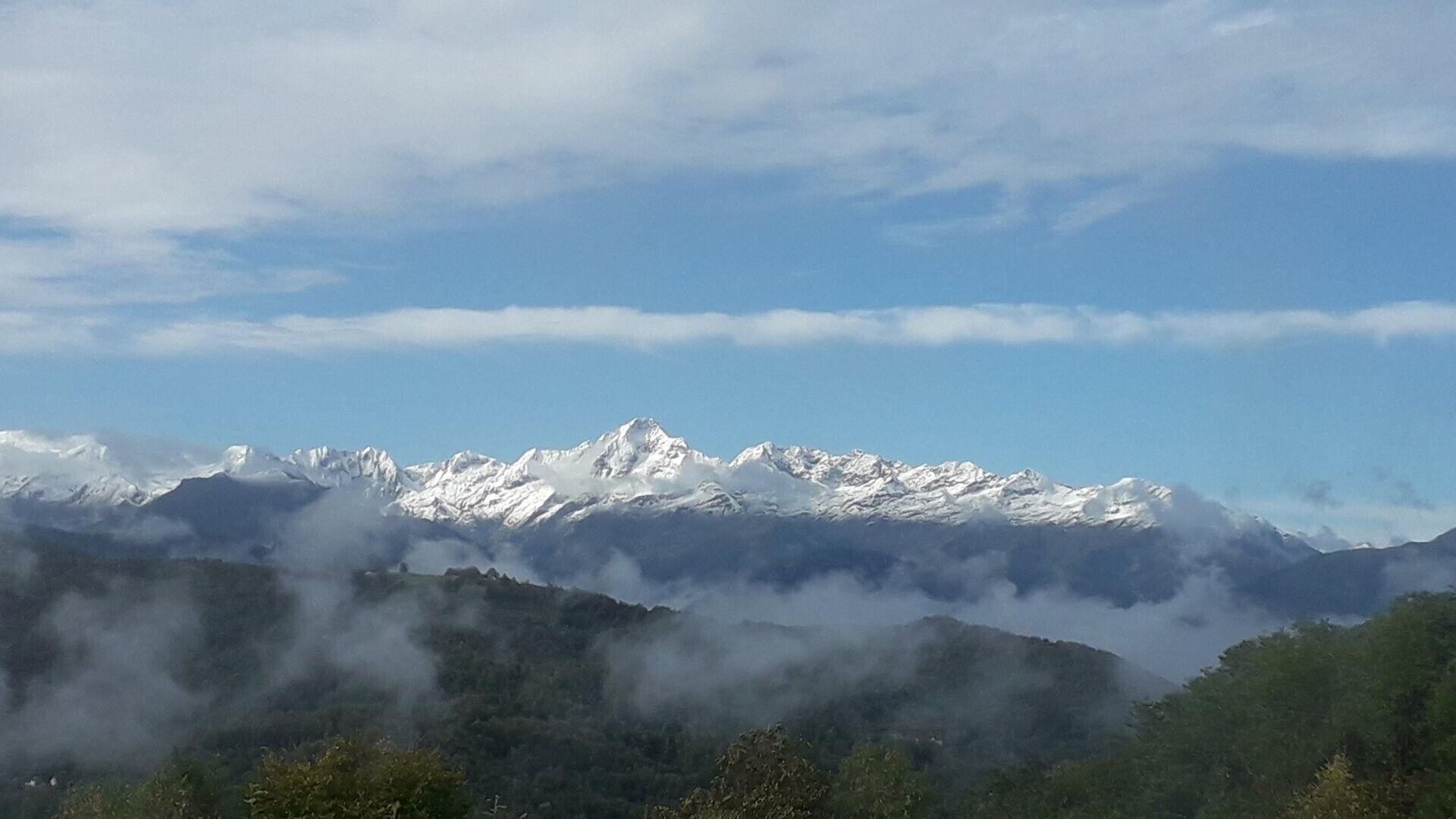 Une chaîne de montagnes aux sommets enneigés, surplombant une vallée boisée.