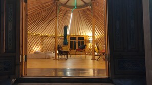 L’intérieur d’une yourte, avec un espace central aménagé en salon, une porte donnant sur l’extérieur et un plancher en bois.