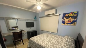 Une chambre à coucher comprenant un lit, un bureau, une chaise, un téléviseur et un appareil de climatisation.