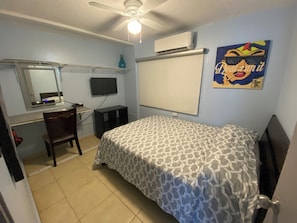 Ein Schlafzimmer mit Bett, Schreibtisch, Stuhl, Fernseher und Klimaanlage.