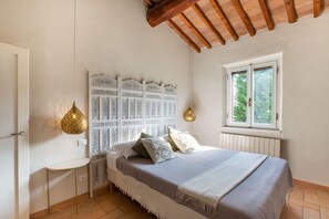 Ein Schlafzimmer mit einem Bett, einem Fenster, einer weißen Wand und einer Decke mit Holzbalken.