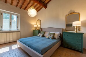 Ein Schlafzimmer mit Bett, Nachttischen, Kommode, einer Kandelaber, einem Fenster und einem Spiegel.