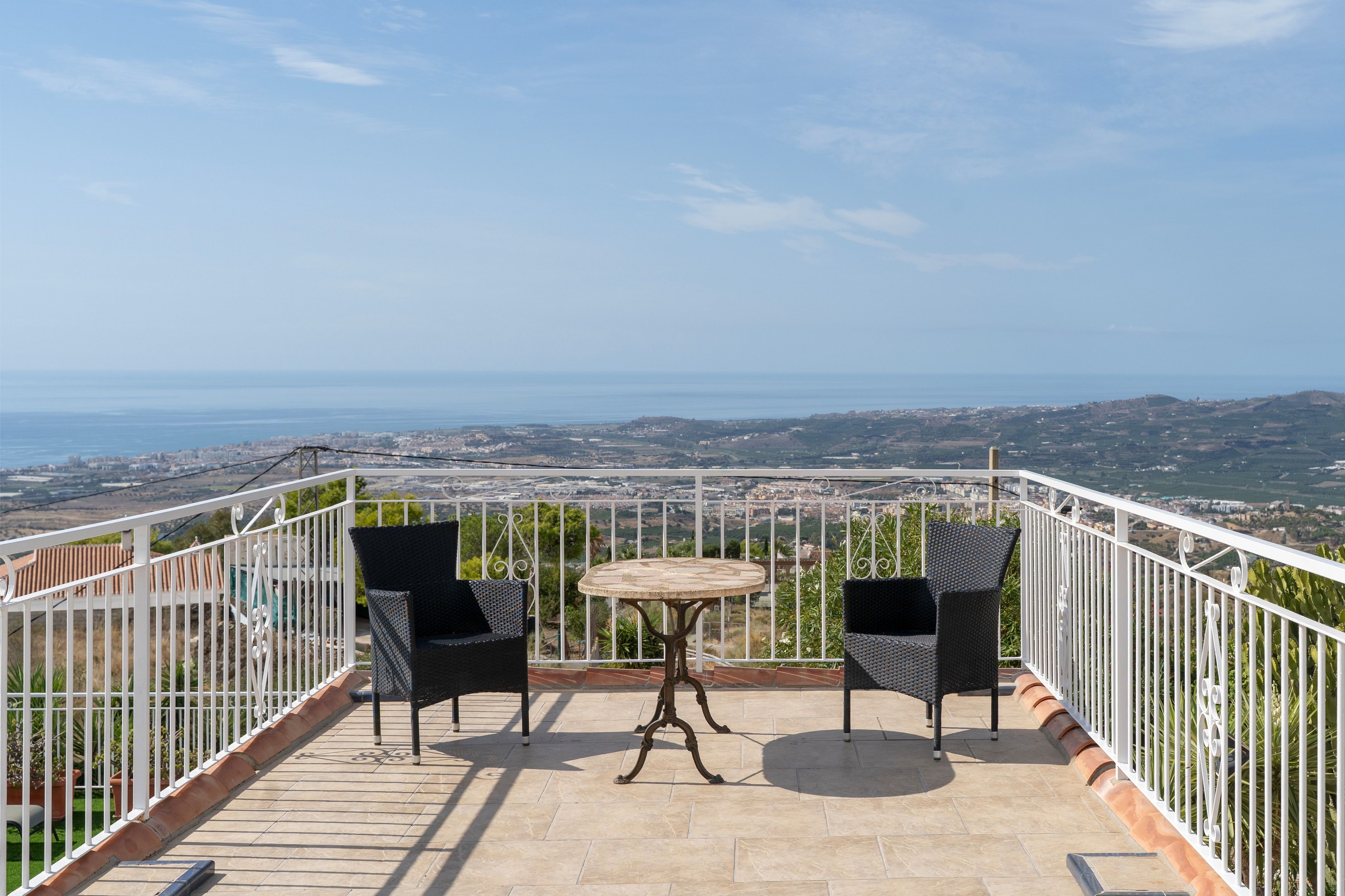 Una terraza con dos sillas y una mesa, con vista a un paisaje costero.
