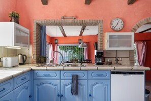 Eine Küche mit blauen Schränken, einer Spüle, einer Uhr und einem Fenster mit Vorhängen.