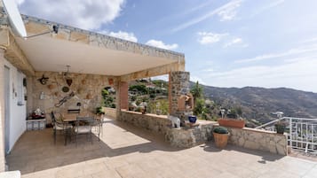 A covered patio with stone walls, a table with chairs, and potted plants.