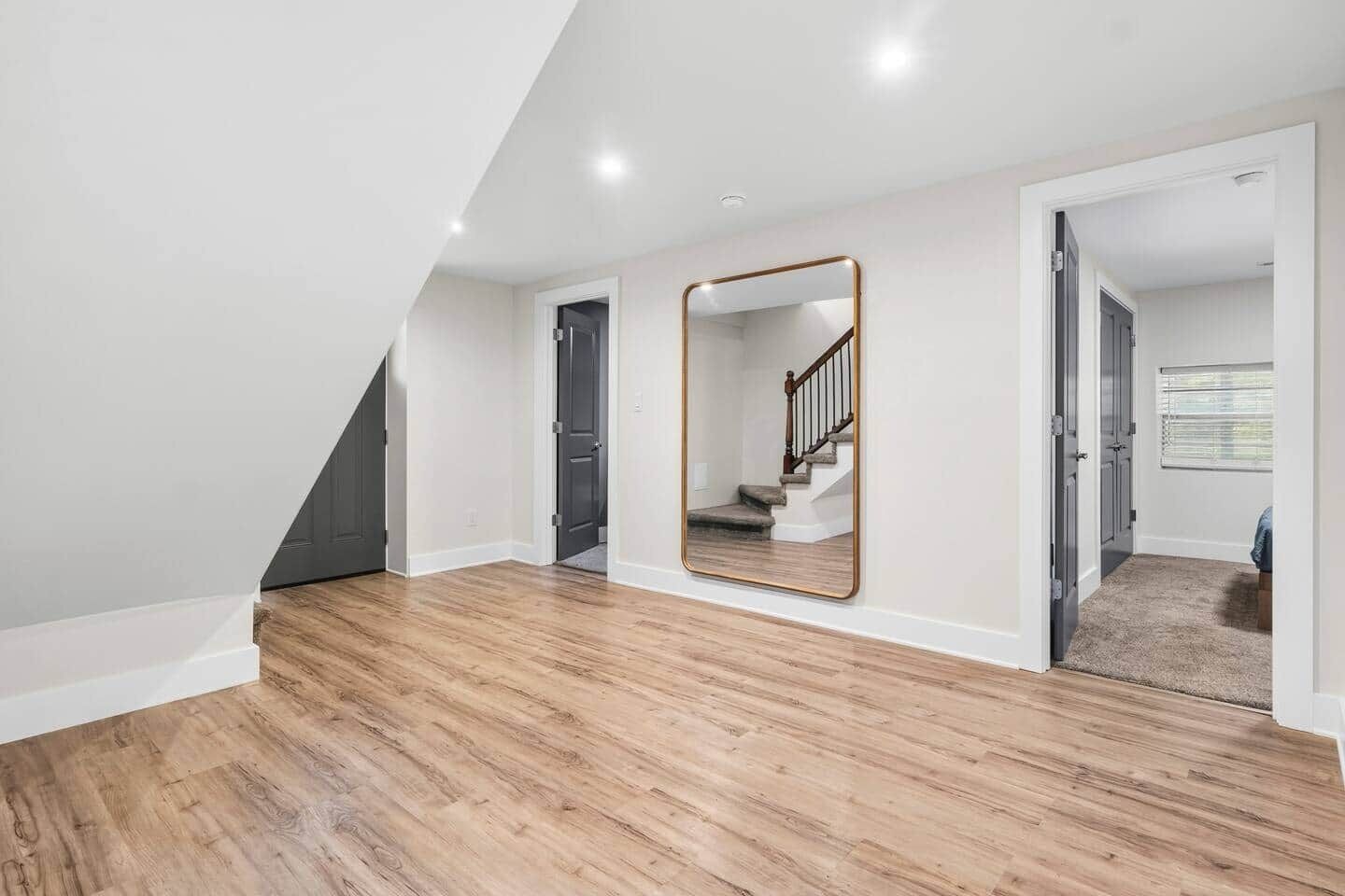 A spacious room with a wooden floor, a large mirror, and a staircase leading to another level.