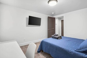 A bedroom with a bed, a desk, a chair, a television on the wall, and a door. - Sanctuary - A Cozy Peaceful Cottage Getaway (Knox County)