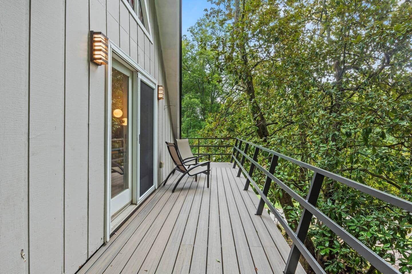 A wooden deck with a chair, a railing, and a building with a window and a door.