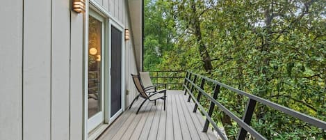 A wooden deck with a chair, a railing, and a building with a window and a door.