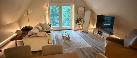 A cozy, well-lit room with a dining table, chairs, a sofa, a television, and a ceiling fan.