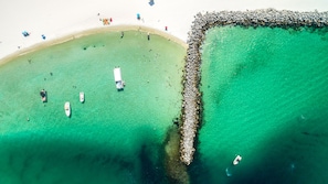An aerial view of a beach with clear turquoise waters, a rocky breakwater, and several boats. - Gorgeous Inside and Views in East Pass Towers 602 (Destin)