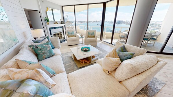 Een moderne woonkamer met een groot raam met uitzicht op een jachthaven, een open haard en een zithoek met een salontafel.