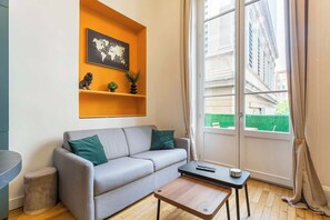 Ein Wohnzimmer mit grauem Sofa, einem kleinen Holztisch und einer Weltkarte an einer Wandregal.