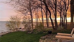 A beachside garden with a wooden bench, a stone pathway, and a view of the ocean. - Lake Erie Retreat (Haldimand)