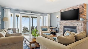 A living room with a fireplace, a television mounted above it, and a large window with a view of the outdoors. - Lake Erie Retreat (Haldimand)