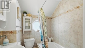 A bathroom with a toilet, sink, bathtub, and a shower curtain. - Lake Erie Retreat (Haldimand)