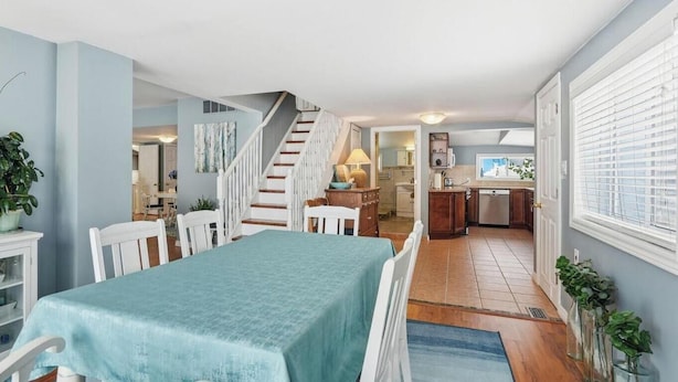 A dining area with a table and chairs, a staircase leading to a kitchen, and a living space with a TV. - Lake Erie Retreat (Haldimand)