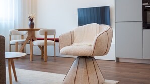 Ein modernes Wohnzimmer mit einem außergewöhnlichen Sessel, ein Essbereich mit Holzkästen und eine Küche mit blauer Akzentwand.