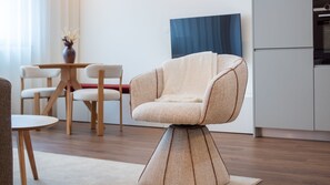 Una sala moderna con una silla original, un comedor con sillas de madera y una cocina con un muro azul decorativo.