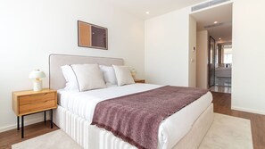 Un dormitorio moderno con cama, mesitas de noche, lámpara de noche, manta decorativa y un cuadro en la pared.