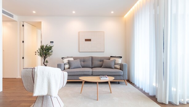 Ein modernes Wohnzimmer mit einem grauen Sofa, einem runden Couchtisch und einem weißen Sessel.