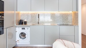 Eine kompakte Küche mit eingebauter Waschmaschine, Spüle und einer Arbeitsplatte mit Wasserkocher und Kaffeemaschine.