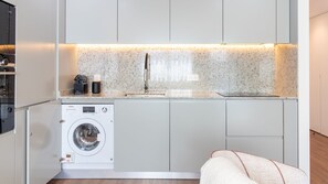 Cocina compacta con lavadora integrada, un lavamanos y una encimera con tetera y cafetera.