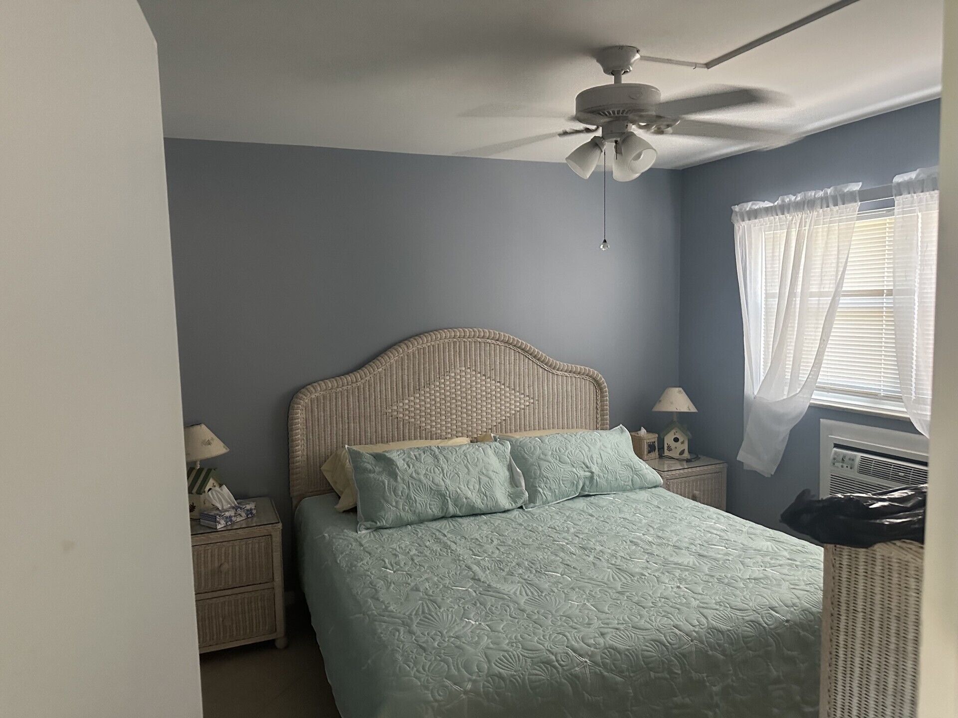 A bedroom with a bed, a nightstand, a ceiling fan, a window with curtains, and a wall heater.