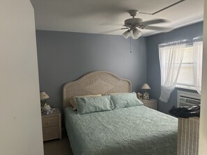 A bedroom with a bed, a nightstand, a ceiling fan, a window with curtains, and a wall heater. - Wonderful first floor 2-bedroom condo with AC in beautiful Marco Island (Marco Island)