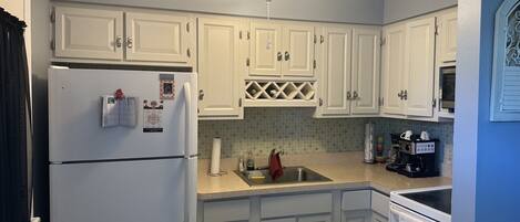 A kitchen with white cabinets, a refrigerator, a ceiling fan, and a coffee maker.