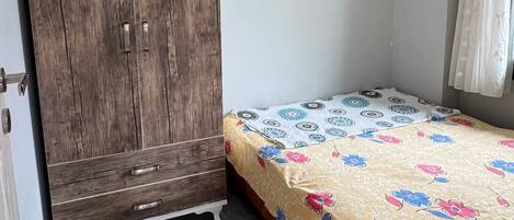 A bedroom with a bed, a wardrobe, and a window with curtains.
