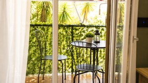 Un balcone con ringhiera in metallo, due sedie, un tavolino, una pianta in vaso e una lanterna.