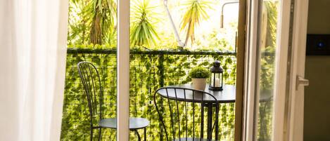 A balcony with a metal railing, two chairs, a small table, a potted plant, and a lantern.
