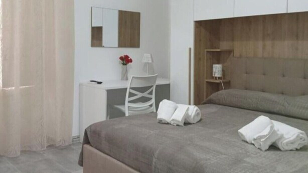Een slaapkamer met een bed, een bureau, een stoel, een nachtkastje en een spiegel.