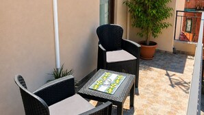 Een terras met rieten meubilair, een plant in pot en een betegelde vloer.
