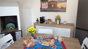 Een eetgedeelte met een houten tafel, stoelen, een vaas met zonnebloemen en een schilderij van een gebouw aan de muur.
