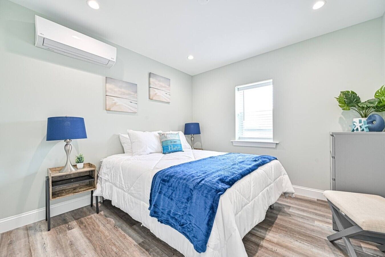 Quarto com cama, mesas de cabeceira, janela e uma planta.