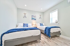 Ein Schlafzimmer mit zwei Betten, einem Fenster und einem kleinen Tisch mit Lampe.