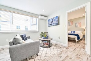 Ein modernes Wohnzimmer mit einem grauen Sofa, einem runden Couchtisch und einem großen Fenster mit Jalousien.