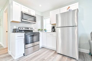 A modern kitchen with stainless steel appliances, white cabinetry, and a wooden floor. - Salty Shore Oasis: Spectacular Retreat (Wildwood)