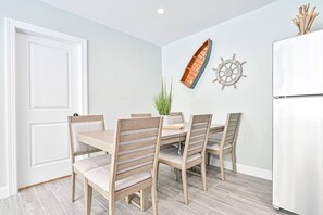 A dining area with a wooden table and chairs, a potted plant, and nautical-themed wall decor. - Seaside Serenity: Salty Shore Retreat (Wildwood)