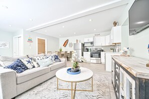 A modern living room with a sofa, coffee table, and kitchen area with cabinets and appliances. - Seaside Serenity: Salty Shore Retreat (Wildwood)